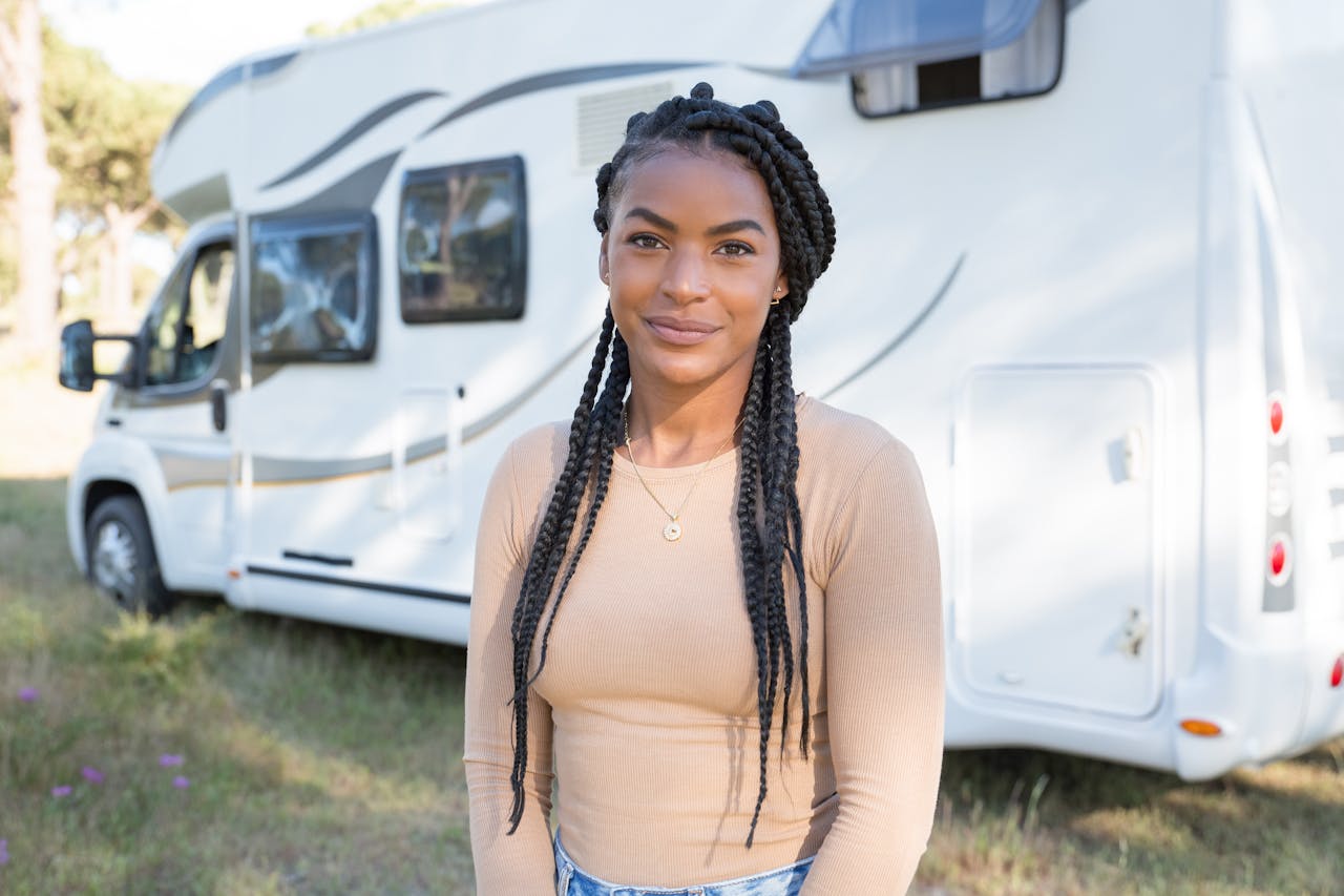 Portrait of a smiling woman outdoors with a camper van in a sunny setting.